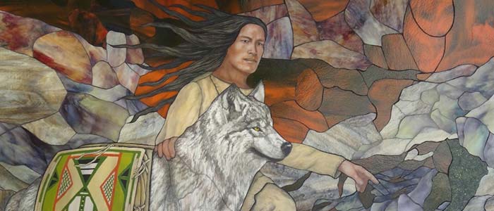 Native American man crouched behind a wolf that is wearing parfleche saddle bags