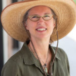 Headshot of artist Terri Wells in a straw hat and green shirt